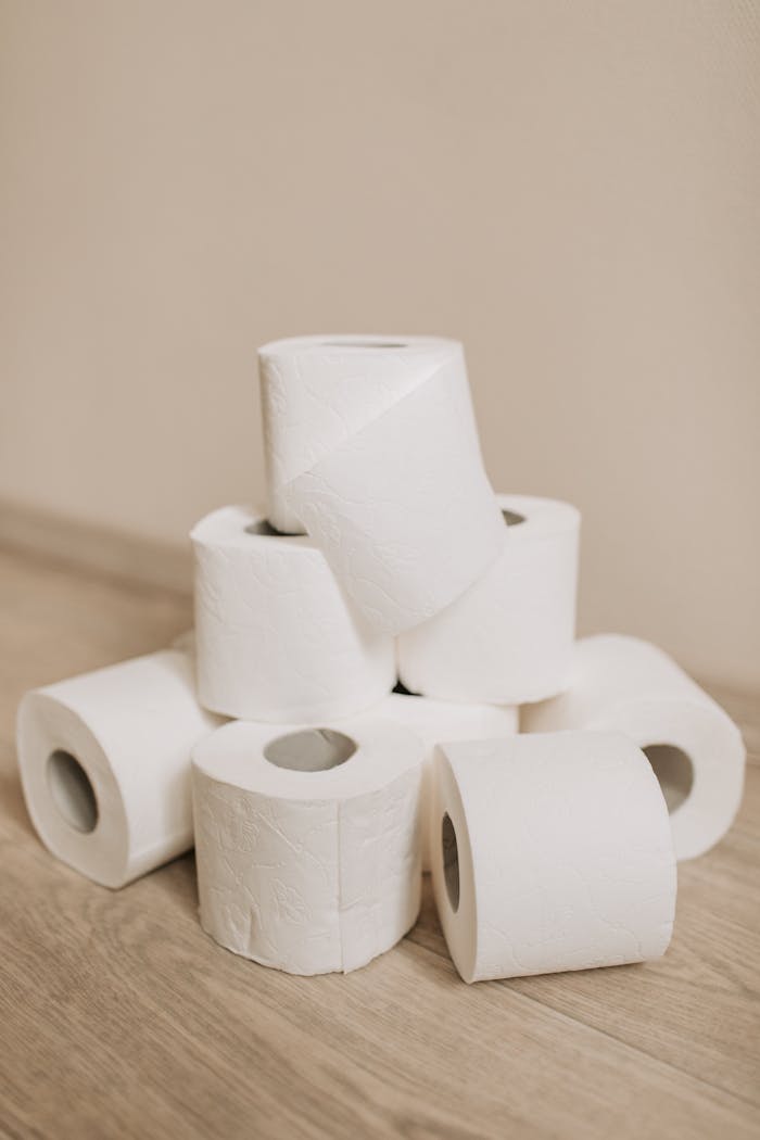 A neat pile of white toilet paper rolls arranged on a wooden floor indoors.
